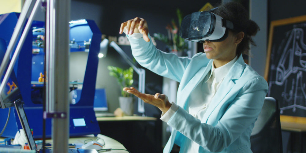 Woman wearing VR headset while working with engineering projects in a lab with three dimensional printing.