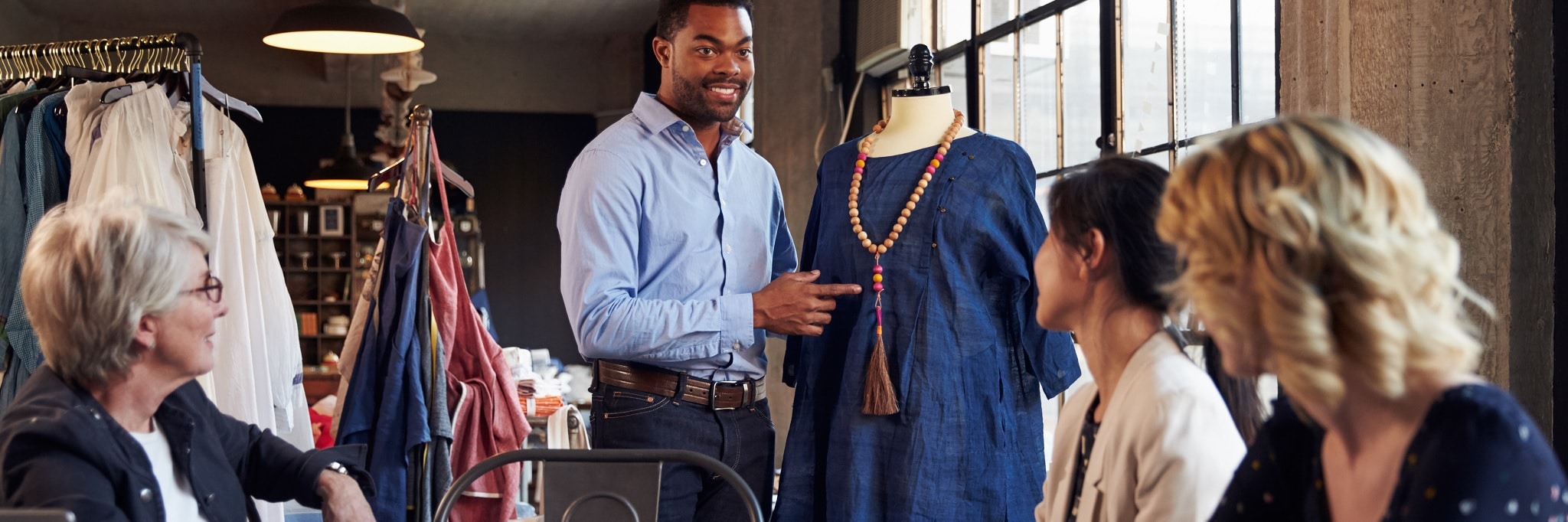 Young male fashion professional presenting a dress with a necklace on a dressmakers mannequin to older female fashion designers
