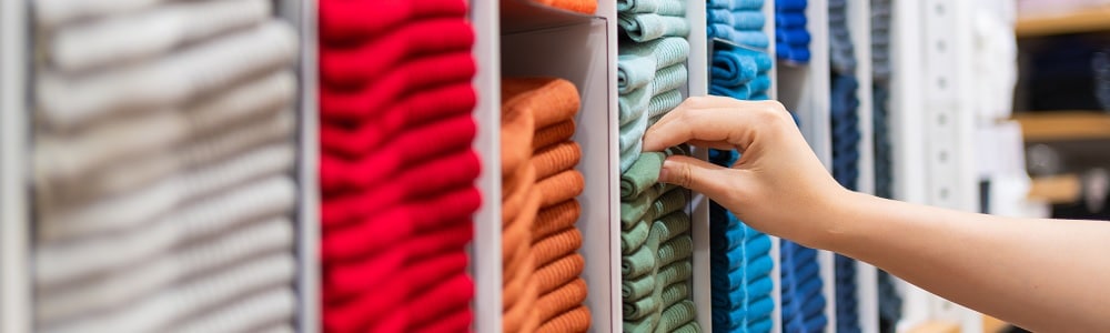 A selection of coloured cotton fabrics in grey, red, orange, green, light blue and dark blue organised into sections with the hand of a fashion research manager reaching out to choose the green fabric at the Leeds School of Design.