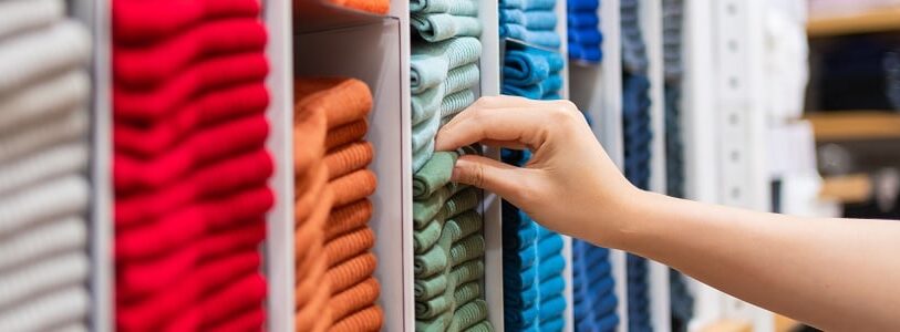 A selection of coloured cotton fabrics in grey, red, orange, green, light blue and dark blue organised into sections with the hand of a fashion research manager reaching out to choose the green fabric at the Leeds School of Design.