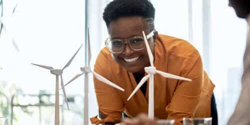 A bespectacled person smiling, lowering to look at models of windmills